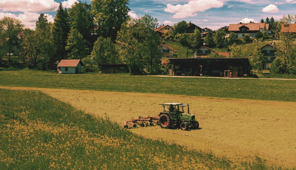 Campo agrícola verde de primavera con tractor, representando bienes raíces y financiamiento de tierra para agricultura.