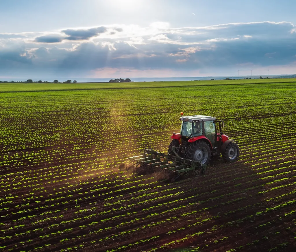 A red tractor working a wide agricultural field under the sun, illustrating the need to finance agricultural equipment and machinery.